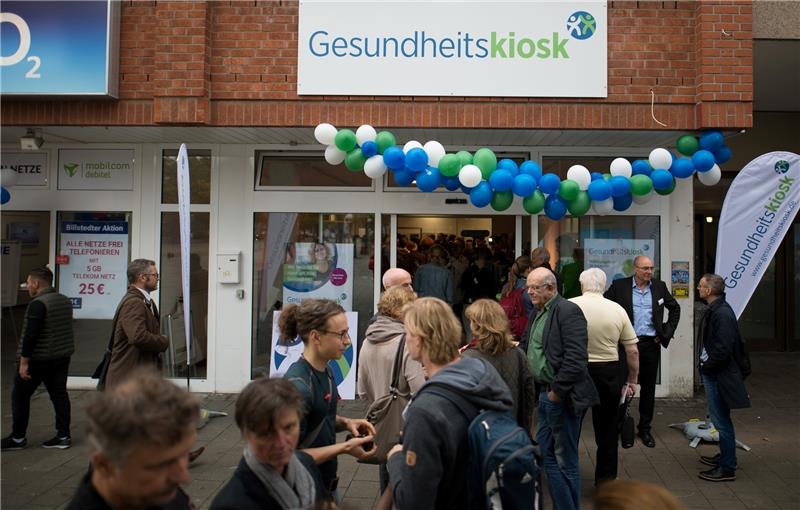 Passanten und Teilnehmer der Eröffnungsfeier stehen vor dem neuen Gesundheitskiosk in Hamburg. Foto Reinhardt/dpa