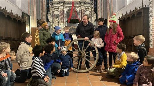Pastor Haase erklärt den Kindern der Krippenspielgruppe, was das alte Wagenrad mit dem heutigen Adventskranz zu tun hat.