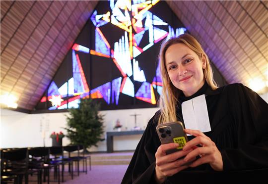 Pastorin Josephine Teske sitzt mit ihrem Smartphone in der Dietrich-Bonhoefer-Kirche der Gemeinde Meiendorf-Oldenfelde. Seit 2019 begeistert die Pastorin Menschen mit ihrem Instagram-Account „Seligkeitsdinge" für den Glauben. Foto: Christian Charisius/dpa