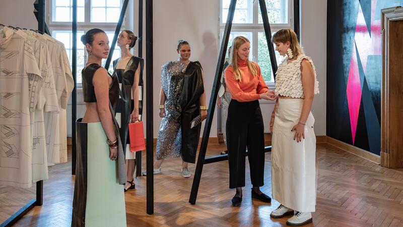 Schülerinnen stellen die Modewerke von Künstlerin Maria Visser zur Schau, die vor der Performance zur Eröffnung noch einmal prüft, ob die Kleidungsstücke richtig sitzen
