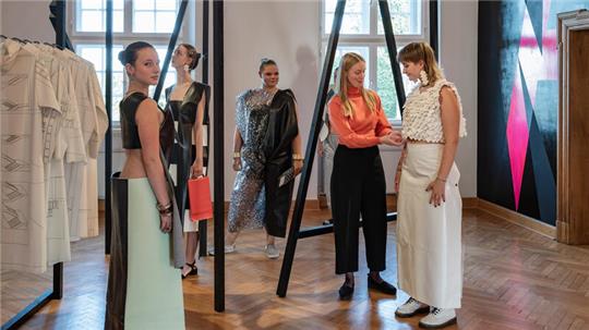 Schülerinnen stellen die Modewerke von Künstlerin Maria Visser zur Schau, die vor der Performance zur Eröffnung noch einmal prüft, ob die Kleidungsstücke richtig sitzen