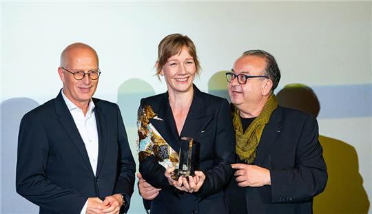 Peter Tschentscher (l-r, SPD), Erster Bürgermeister von Hamburg, Schauspielerin Sandra Hüller mit ihrem Preis und Albert Wiederspiel, scheidender Leiter vom Filmfest Hamburg. Die Schauspielerin Sandra Hüller hat auf dem Filmfest Hamburg den Douglas-Sirk-Preis überreicht bekommen. Foto: Jonas Walzberg/dpa