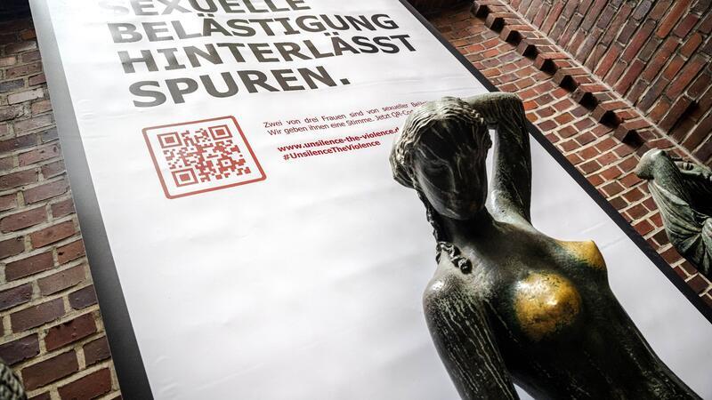 Plakat mit der Aufschrift „Sexuelle Belästigung hinterlässt Spuren“ hinter der Bronzeskulptur „Jugend“ von Bernhard Hoetger in Bremen.