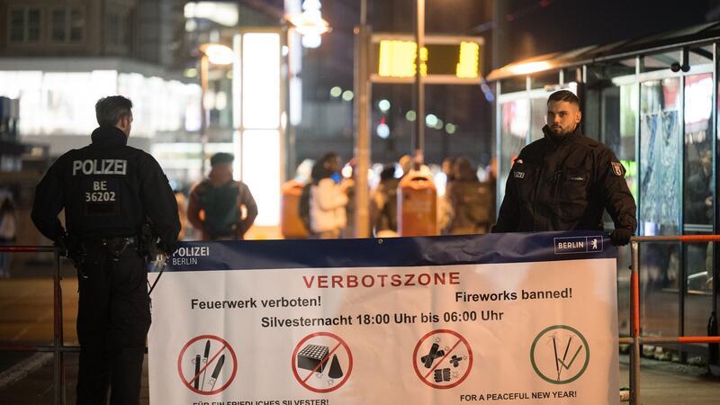 Angriffe auf Polizei, Hunderte Festnahmen in Berlin Polizeibeamte stehen an einem Plakat, das auf die Böllerverbotszone am Berliner Alexanderplatz hinweist.