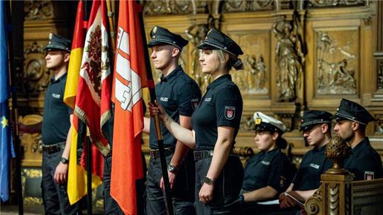 Polizeibeamte stehen im Hamburger Rathaus bei ihrer Vereidigung mit Flaggen in der Hand.