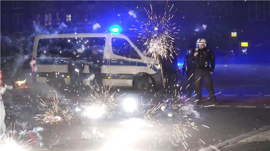 Polizeibeamte stehen in der Silvesternacht 2022 in Berlin hinter explodierendem Feuerwerk.