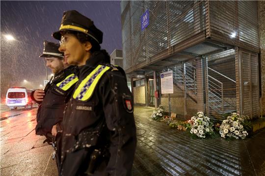 Polizeibeamte stehen vor dem Gebäude der Zeugen Jehovas im Stadtteil Alsterdorf, vor dem zuvor Kränze in Gedenken an die Opfer eines Amoklaufs niedergelegt wurden. Bei einem Amoklauf während einer Veranstaltung der Zeugen Jehovas sind am Donnerstagabend mehrere Menschen getötet und einige Personen verletzt worden. Foto: Christian Charisius/dpa