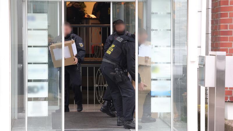 Polizeibeamte tragen in Kartons sichergestelltes Material aus einem Gebäude.