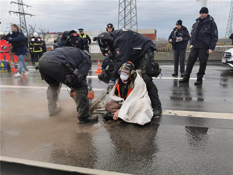 Polizisten fräsen einen Klimaaktivisten frei, der sich auf einer Brücke festgeklebt hat. Foto: Steven Hutchings/TNN/dpa