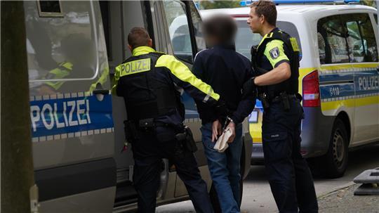 Polizisten führen einen Jugendlichen zu einem Polizeiauto. (Symbolbild)