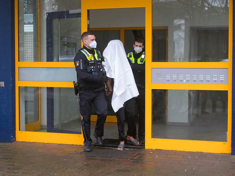 Polizisten führen einen Tatverdächtigen in Handschellen aus dem Haus. Eine Frau ist am Sonntag mit lebensgefährlichen Stichverletzungen in Hamburg-Niendorf aufgefunden worden. Foto: Jonas Walzberg/dpa