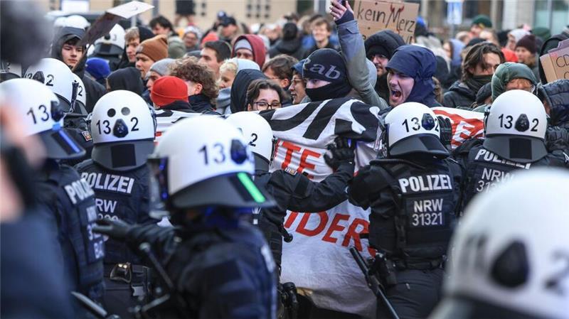 Polizisten schieben an der Uniklinik in Köln Demonstranten beiseite, um die Abfahrt von CDU-Chef Merz zu ermöglichen. 