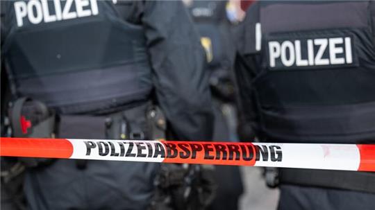 Polizisten stehen hinter einem Polizei-Flatterband.