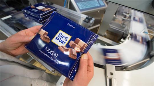Eine Mitarbeiterin des Schokoladenherstellers Ritter Sport prüft die Verpackung einer Tafel Schokolade.