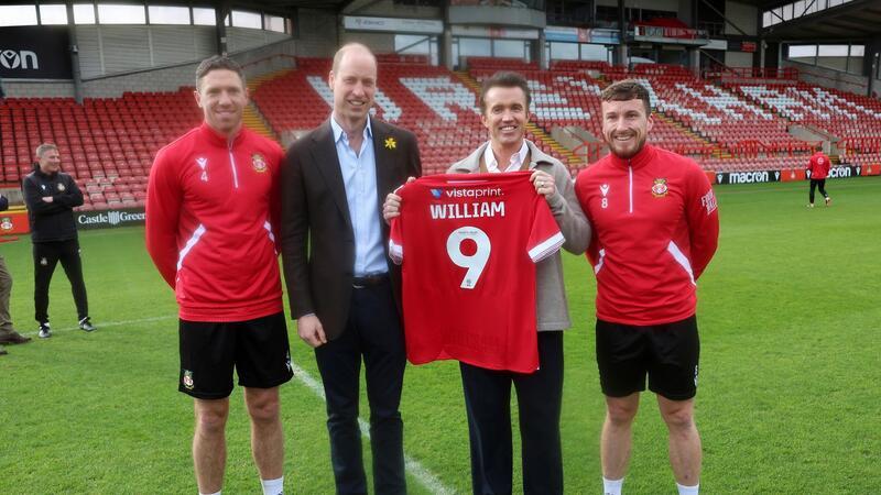 Prinz William (2.v.l) mit Rob McElhenney (2.v.r), Co-Eigentümer des Viertligisten AFC Wrexham, und den Spielern Ben Tozer (l) und Luke Young auf dem Spielfeld des Racecourse Ground, der Heimstätte von Wrexham AFC.
