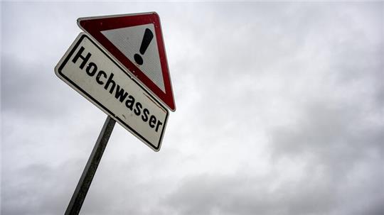 Ein Schild warnt vor Hochwasser, der Himmel über ihm verheißt weiteren Regen. 
