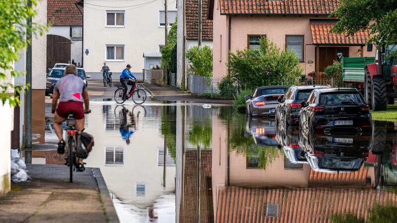 Klimawandel verschlimmerte Hochwasser Radler fahren durch eine überflutete Straße. Im Bereich der Gemeinde Baar-Ebenhausen war ein Damm an zwei Stellen geborsten.
