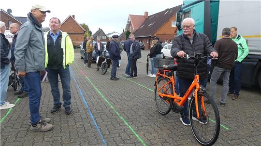 Radler sollen auf der Straße fahren. Kreidestreifen symbolisieren die künftigen Breiten von Fußweg und Radstreifen auf der L111. Daneben (rechts) fahren Lkw und Pkw im Gegenverkehr: Es wird eng.