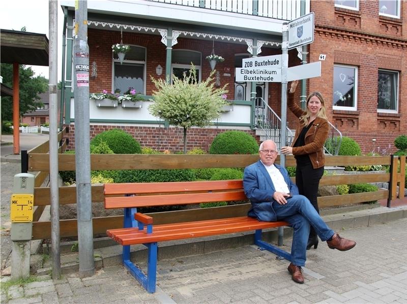 Ratsherr Robert Kamprad sitzt auf der neuen Mitfahrerbank in Hedendorf Probe, Ortsbürgermeisterin Birgit Butter dreht das Mitfahrschild „ZOB Buxtehude“ in Position. Foto Richter