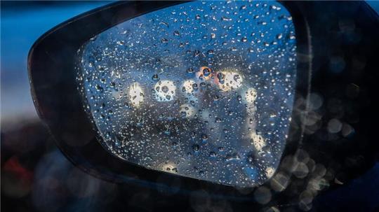 Regentropfen sind am Morgen im Berufsverkehr auf einem Rückspiegel an einem Auto zu sehen.
