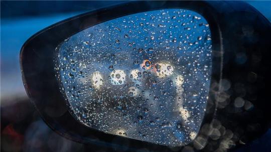 Regentropfen sind am Morgen im Berufsverkehr auf einem Rückspiegel an einem Auto zu sehen.