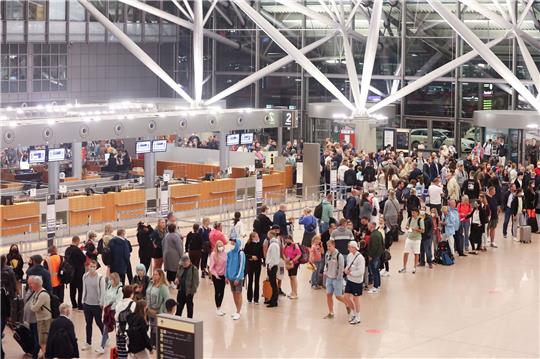 Reisende stehen am Morgen in einer Schlange  die zur Sicherheitskontrolle am Hamburger Flughafen führt. In Hamburg haben die Ferien begonnen.