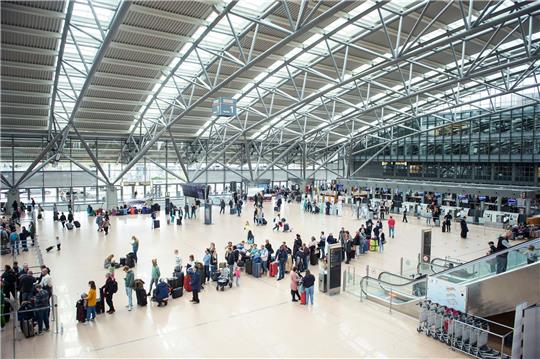 Reisende stehen im Terminal des Flughafen Hamburg mit ihrem Gepäck in einer Warteschlange an einem Check in-Schalter.