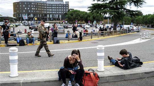 Reisende warten, während ein französischer Soldat vor dem Flughafen Toulouse-Blagnac patrouilliert.