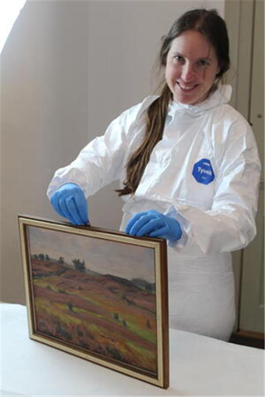 Restauratorin Jasmin Wollenhaupt begutachtet das Gemälde „Hügelgrab Nr. 18 auf dem Langenberg bei Sassenholz“ von Emil Schache.