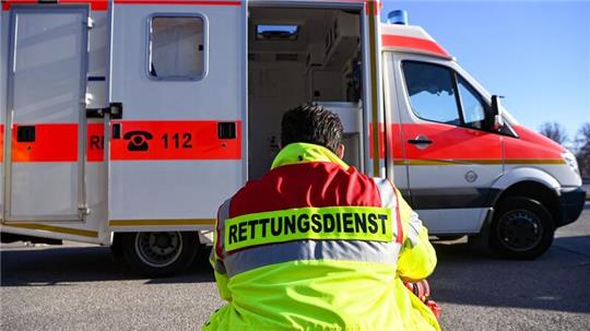 „Rettungsdienst“ steht auf der Jacke eines Mannes vor einem Rettungswagen der Feuerwehr.