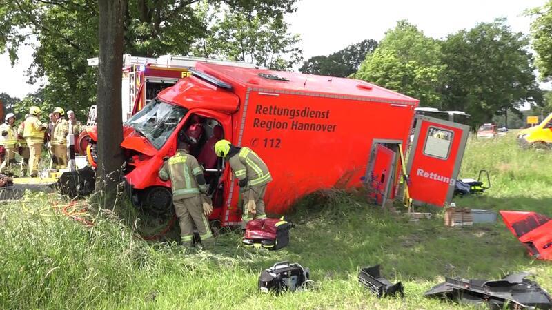 Rettungswagen verunglückt bei Einsatz: Zwei Rettungskräfte schwer verletzt Rettungskräfte stehen neben einem Krankenwagen, der gegen einen Baum geprallt ist.