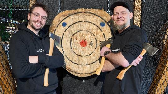 Romain Félix (l), Gründer aus Belgien, und Jim Barker, Axe Master, stehen vor einer Zielscheibe im Woodcutter im Othmarscher Park.