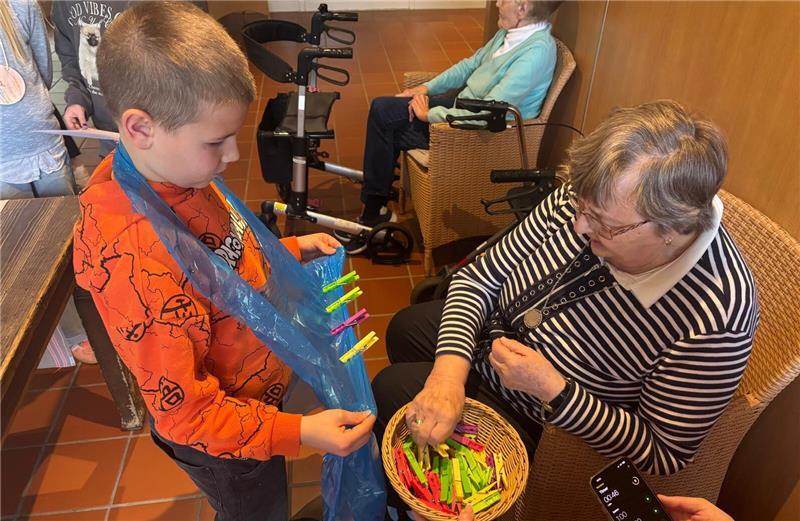 Rosemarie Lamek muss so viele Klammern wie möglich an die Schürze von Grundschüler Dean klammern.