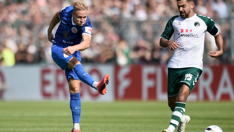 3. Liga: Wiesbaden verpflichtet Lübecker Gözüsirin Rostocks Kai Pröger (l) schießt an Lübecks Tarik Gözüsirin vorbei auf das Lübecker Tor.