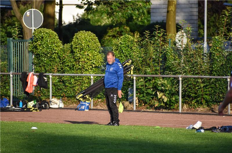 Trainer Björn Mielke hat Fußballtore unter seinem Arm und schaut seiner Mannschaft beim Trainieren zu.