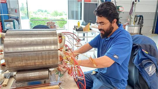 Saberi hat eine Ausbildung zum Elektrotechniker absolviert. Hier sitzt er im Betrieb am Pitchmotor, der in einem Rotorblatt von einer Windkraftanlage eingesetzt wird.