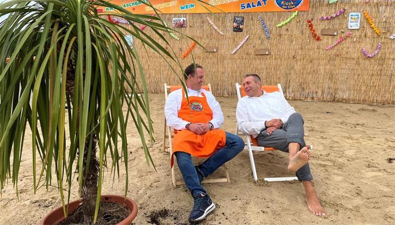 Samtgemeindebürgermeister Timo Gerke (rechts) nimmt Platz im Schatten der Palmen. Vor seinem Imbiss hat Mirko Rischmüller einen Beachclub eingerichtet.