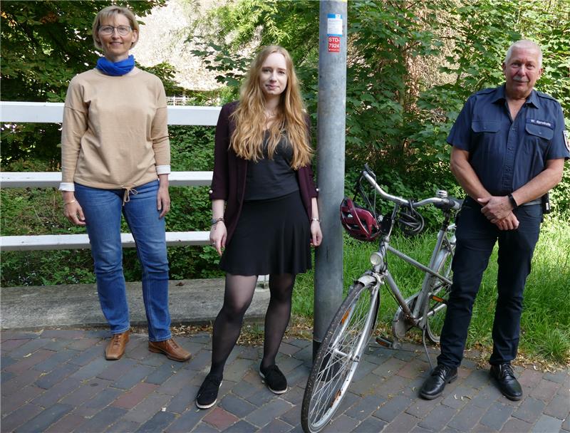 Sandra Junge vom Tourismusverband, Charlene Friedrich aus dem Planungsamt und Wilfried Sprekels (von links), Leiter der Feuerwehr- und Rettungsleitstelle, an dem Notrufaufkleber an der Brückean der Museumsinsel in Stade. Foto: Landkreis Stade