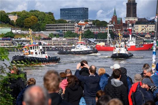 Schaulustige beobachten mehrere Schlepper beim traditionellen Schlepperballett auf der Elbe vor den Landungsbrücken. Vier Schlepper, bis zu 3000-PS-starke und wendige Boote, haben für das nach Angaben der Stadt weltweit einmalige Spektakel zu klassischer Musik auf dem Wasser gewissermaßen getanzt. Foto: Jonas Walzberg/dpa