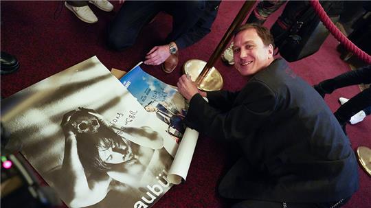 Schauspieler Lars Eidinger schreibt nach dem Fotocall des Films "Lars Eidinger - Sein oder nicht sein" im Rahmen des 30. Filmfests Hamburg im Passage Kino auf dem Boden knieend Autogramme für die wartenden Fans. Foto: Marcus Brandt/dpa