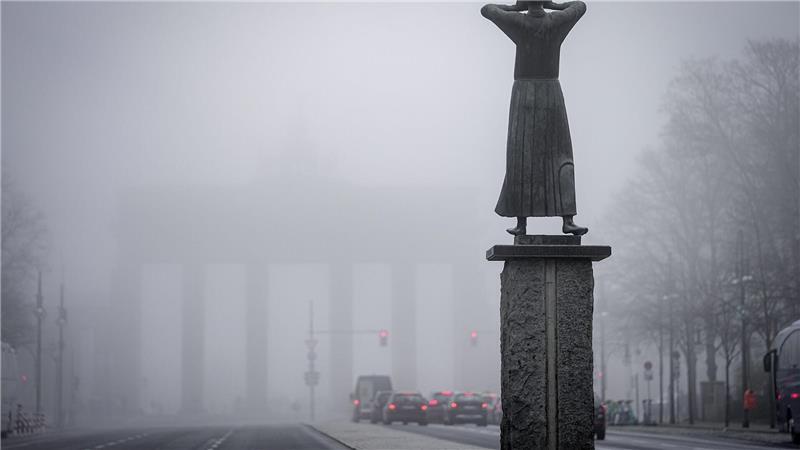 Schemenhaft ist das Brandenburger Tor im Nebel im Hintergrund der Bronzefigur „Der Rufer“ von Gerhard Marcks am frühen Morgen zu sehen.
