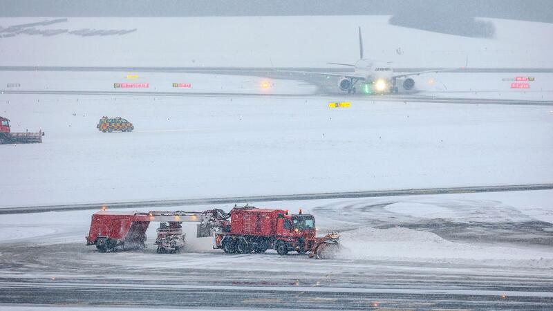 Schnee wird am Flughafen Hamburg geräumt. Im Hintergrund ist eine gelandete Lufthansa-Maschine zu sehen.