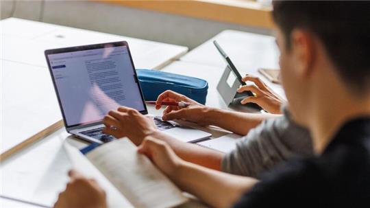 Schüler eines Gymnasiums sitzen vor einem Computer und benutzen ein KI-Tool.