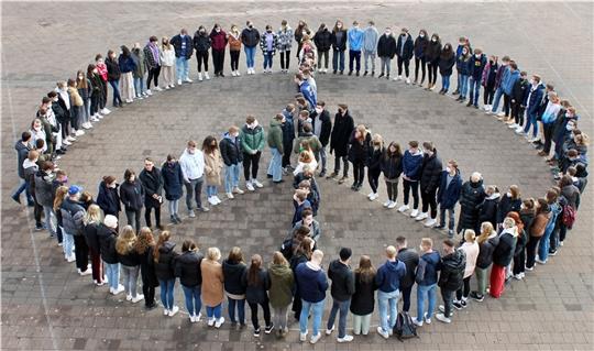 Schüler und Schülerinnen der beiden Oberstufenjahr- gänge 12 und 13 des Aue-Geest-Gym- nasiums in Harsefeld bilden ein mensch- liches Peace- Symbol und legen zum Gedenken an die Menschen in der Ukraine eine Schweige- minute ein. Foto: AGG