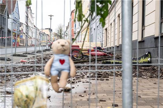 Schutt liegt hinter Absperrgittern, an denen unter anderem ein Kuscheltier angebracht ist. Nach dem tragischen Brand in einem Mehrfamilienhaus in Flensburg am Donnerstag haben Menschen an den Absperrgittern Blumen und Kuscheltiere hinterlassen. Foto: Benjamin Nolte/dpa