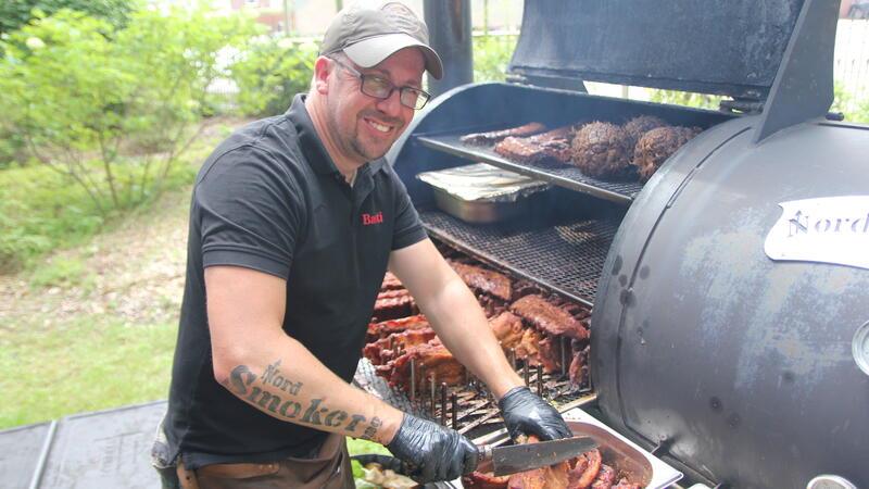 Barbecue-Festival in Himmelpforten: Familiäres Fest feiert das Fleisch Sebastian Jakubowski, der von allen nur „Basti“ genannt wird, bereitet hier Spareribs am Smoker vor und zeigt seine Leidenschaft für Nord Smoker BBQ durch seine Tätowierung am Unterarm.