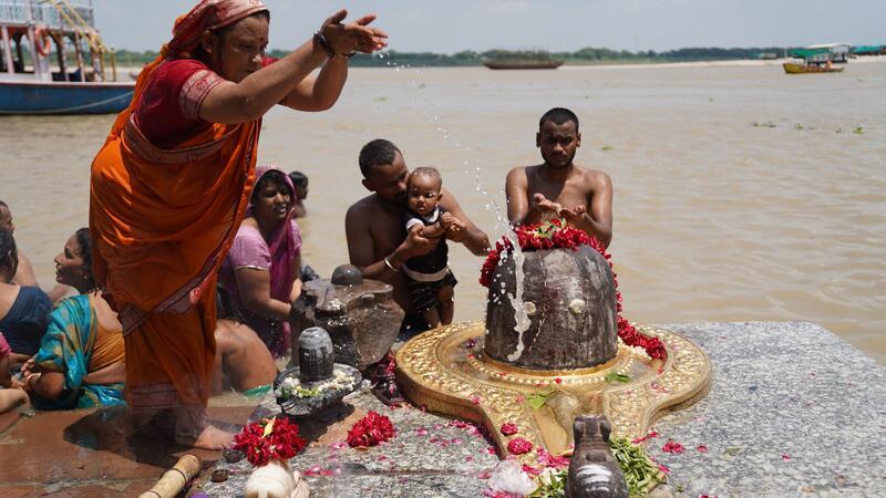 Sharmila und Familienangehörige baden neben einem Symbol von Gott Shiva im Ganges, nachdem sie dort auch die Asche ihrer Angehörigen versenkt haben.