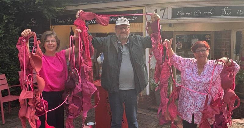 Sie wollen im Oktober die Aufmerksamkeit auf Brustkrebs lenken: Boutique-Inhaberin Beatrice Kietzmann (rechts), ihre Mitarbeiterin Christina Thomas und Peter-Klaus Rambow, Vorstand Netzwerk Männer mit Brustkrebs, halten eine Girlande aus pinkfarbenen BHs. Diese wird im Oktober Straßenschmuck in Buxtehude sein.