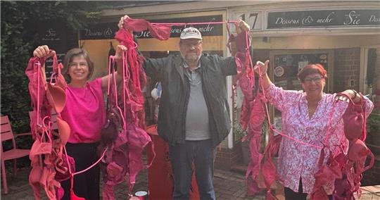 Sie wollen im Oktober die Aufmerksamkeit auf Brustkrebs lenken: Boutique-Inhaberin Beatrice Kietzmann (rechts), ihre Mitarbeiterin Christina Thomas und Peter-Klaus Rambow, Vorstand Netzwerk Männer mit Brustkrebs, halten eine Girlande aus pinkfarbenen BHs. Diese wird im Oktober Straßenschmuck in Buxtehude sein.