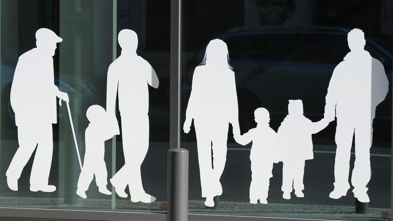 Silhouetten von Menschen in verschiedenem Alter sind auf Fensterscheiben aufgeklebt.